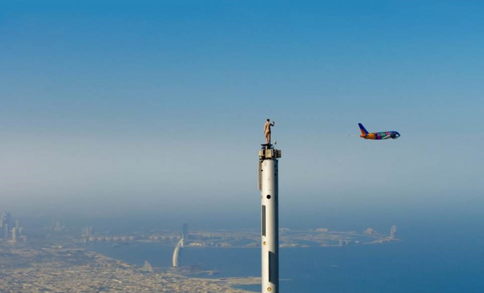 Bild: Doppel-Wow! Mutige Emirates Stuntfrau winkt auf der Spitze des Burj Khalifa, Dubai, dem tieffliegenden A380 im Expo-Design zu. (Bildquelle: Emirates)