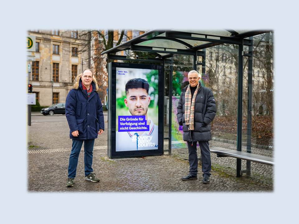 Bild: Kampagnenmotiv neben dem Reichstagsgebäude. Patrick Möller, Geschäftsführer Wall GmbH, und Steffen Baumheier, stellv. Direktor Arolsen Archives, an einem digitalen Werbeträger mit dem Kampagnenmotiv. (Foto: Wall GmbH)